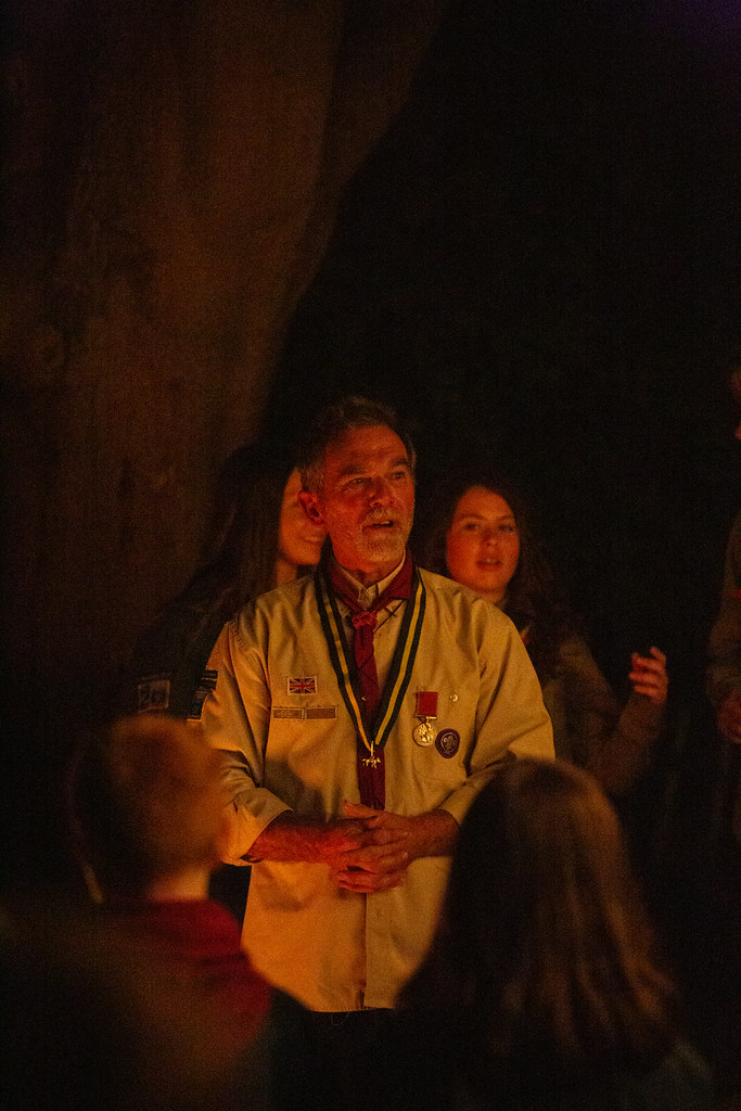 Keith addressing the assembled volunteers and young people, wearing his silver wolf medal. He is lit by the glow of a campfire.